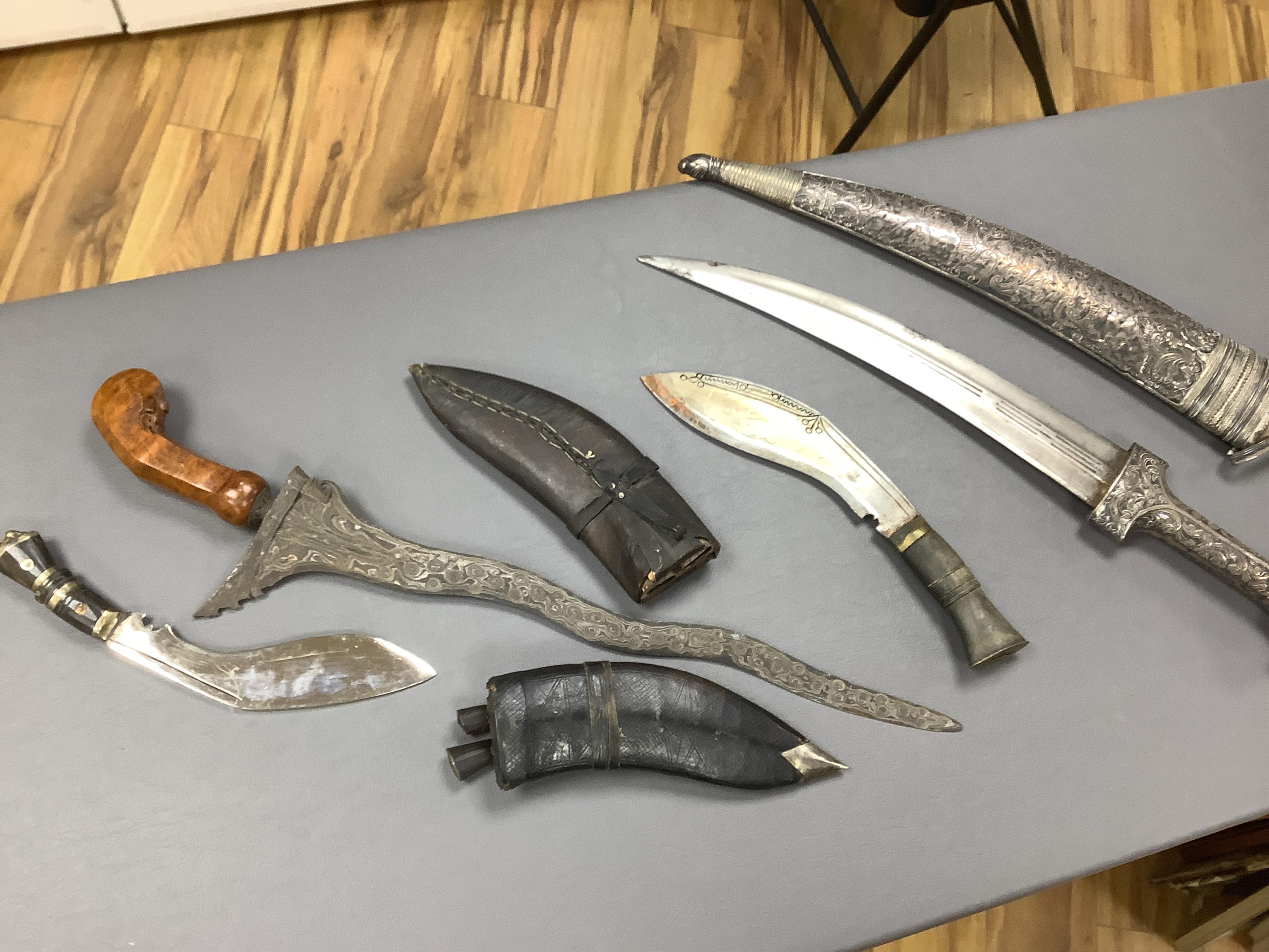 Eighteen assorted world weapons comprising a silver jambya (pommel missing), a knobkerry, a dha, two kris (one with handle missing), a lohar, three kukris, a djambok, a Chinese trousse, a chora, a flyssa, five others and